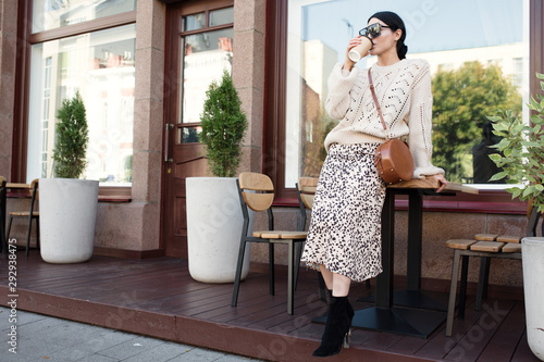 fashion woman in sunglasses and a warm knitted sweater is drinking coffee. Urban atmosphere photo