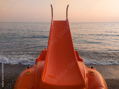 Slide on orange pedal (paddle) boat - pedalo parked on a sandy beach at sunset. Calm blue sea water and clear pink sky in the background. In Canj (Čanj) Montenegro. photo