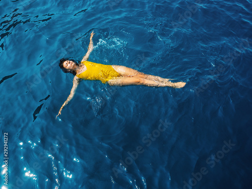 young woman in a one-piece yellow swimsuit floats on the surface of the water.