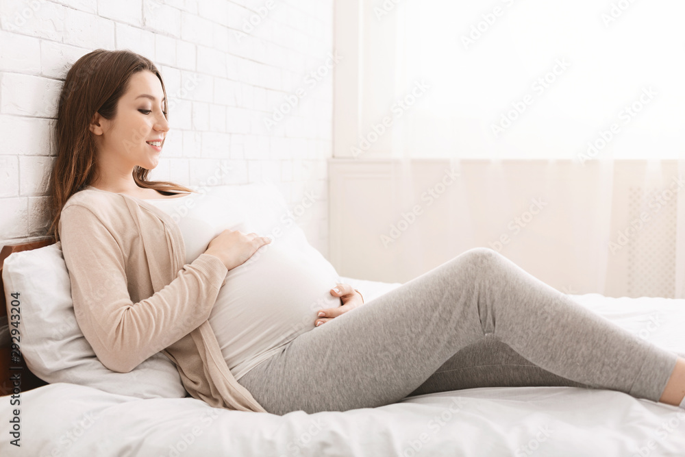 Young expectant woman touching her belly in bed Young expectant woman touching her belly in bed