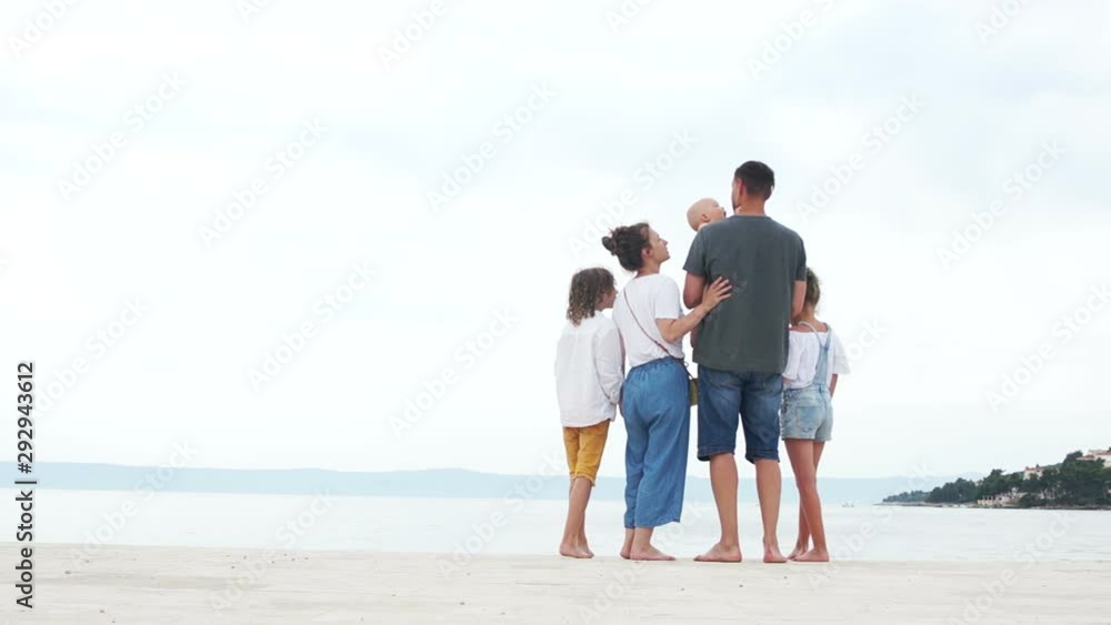 Parents and three children. The kid in his fathers arms reaches out to kiss mom and dad funnyly opening his mouth. A large family is resting on the seashore Parents and three children. The kid in his fathers arms reaches out to kiss mom and dad funnyly opening his mouth. A large family is resting on the seashore