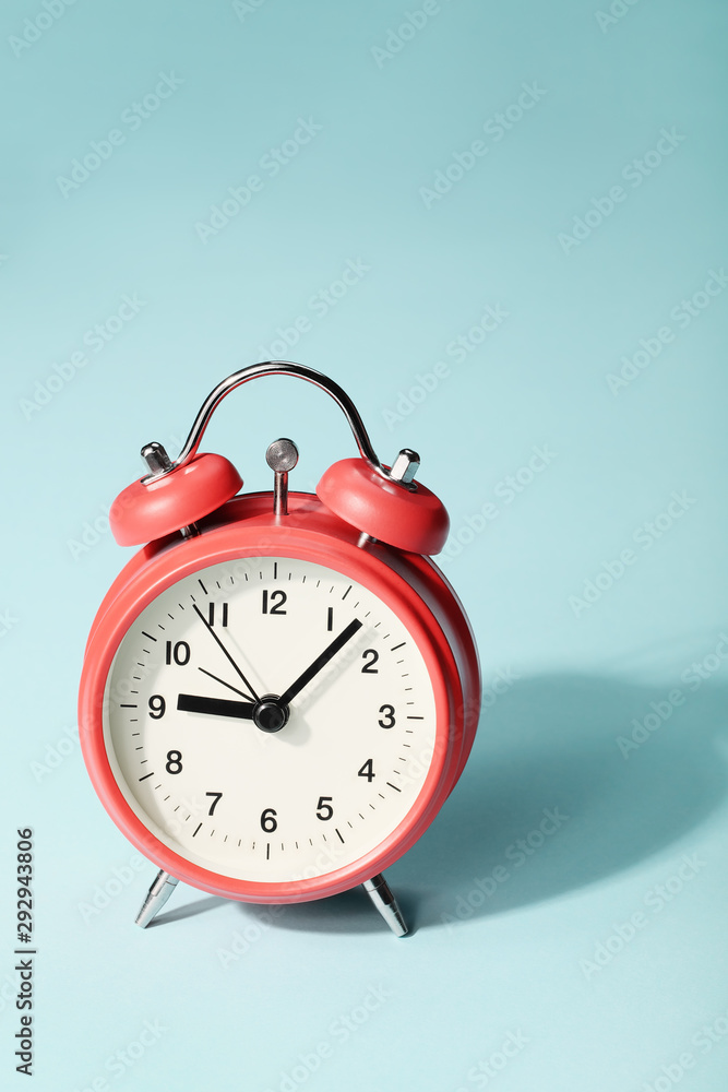 Red alarm clock with shadow on blue background. Seven minutes past nine on the clock Red alarm clock with shadow on blue background. Seven minutes past nine on the clock