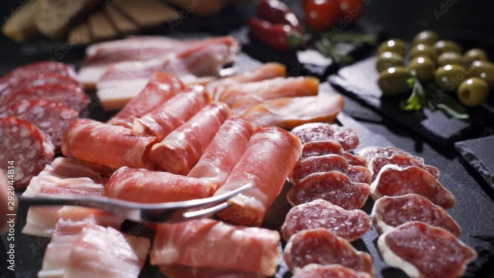 Fork takes a piece of uncooked jerked sausages from a wooden board Fork takes a piece of uncooked jerked sausages from a wooden board