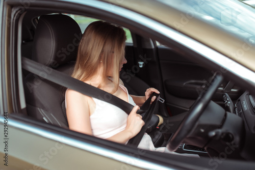 girl car's interior calls on phone, looks in rearview mirror, parks parking lot of shopping center, holds it fastened by steering wheel. Woman in summer sunglasses in city wearing a pink dress.