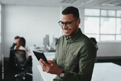 Smiling young businessman touching smartphone and checking online information in the modern office