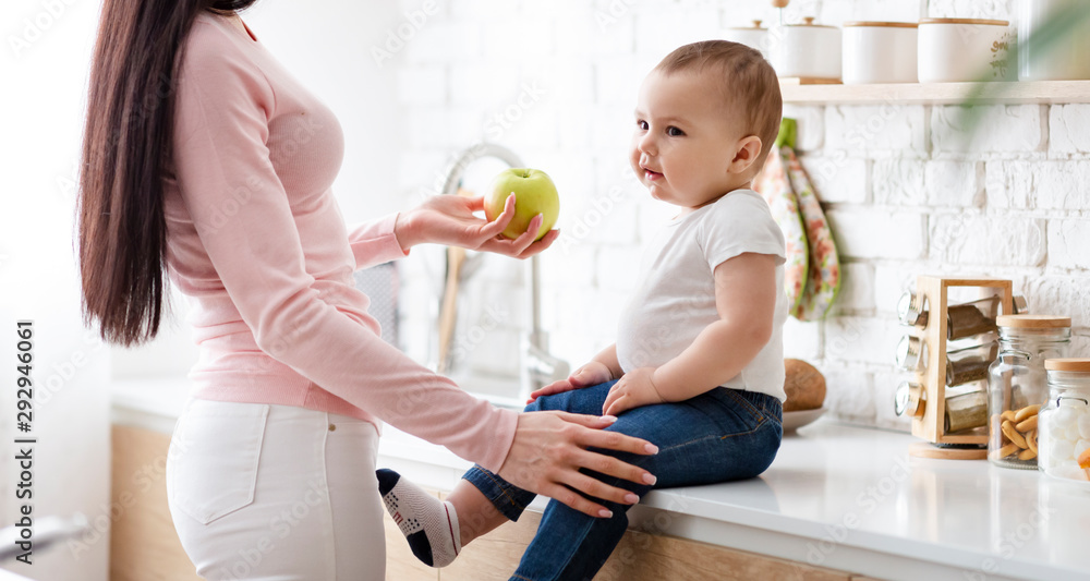 Mom giving fresh apple to little baby son, sitting on kitchentop Mom giving fresh apple to little baby son, sitting on kitchentop