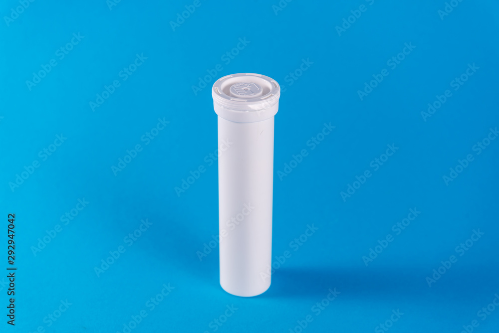 Round white tube with a lid for effervescent tablets, vitamins. New tube with the drug isolated on a blue background. copy space. The concept of health, the treatment of viral diseases and headache Round white tube with a lid for effervescent tablets, vitamins. New tube with the drug isolated on a blue background. copy space. The concept of health, the treatment of viral diseases and headache