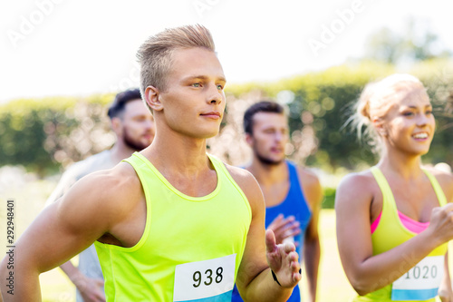 Fototapeta Naklejka Na Ścianę i Meble -  fitness, sport, race and healthy lifestyle concept - group of happy people or sportsmen running marathon with badge numbers at summer park