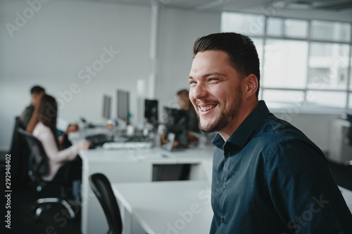 A handsome confident young professional businessman in front of his colleague smiling and looking away at workplace photo