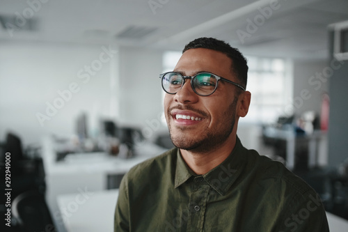 Portrait of a thoughtful smiling young modern business man at office looking away
