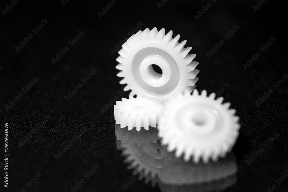 Several white plastic gears on a black mirror background. Mechanical repair. Fix. Reflection. Repair shop. Cogwheels. Elements of a large mechanism. Harmonious work. Several white plastic gears on a black mirror background. Mechanical repair. Fix. Reflection. Repair shop. Cogwheels. Elements of a large mechanism. Harmonious work.