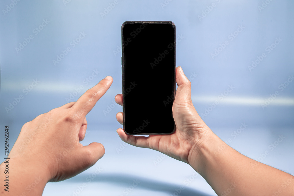 Hand holding Modern mobile smart phone with black screen for mockup on Blue background . Close-up of hands sliding using smartphone are shopping and searching or Selfie on social networks concept  .