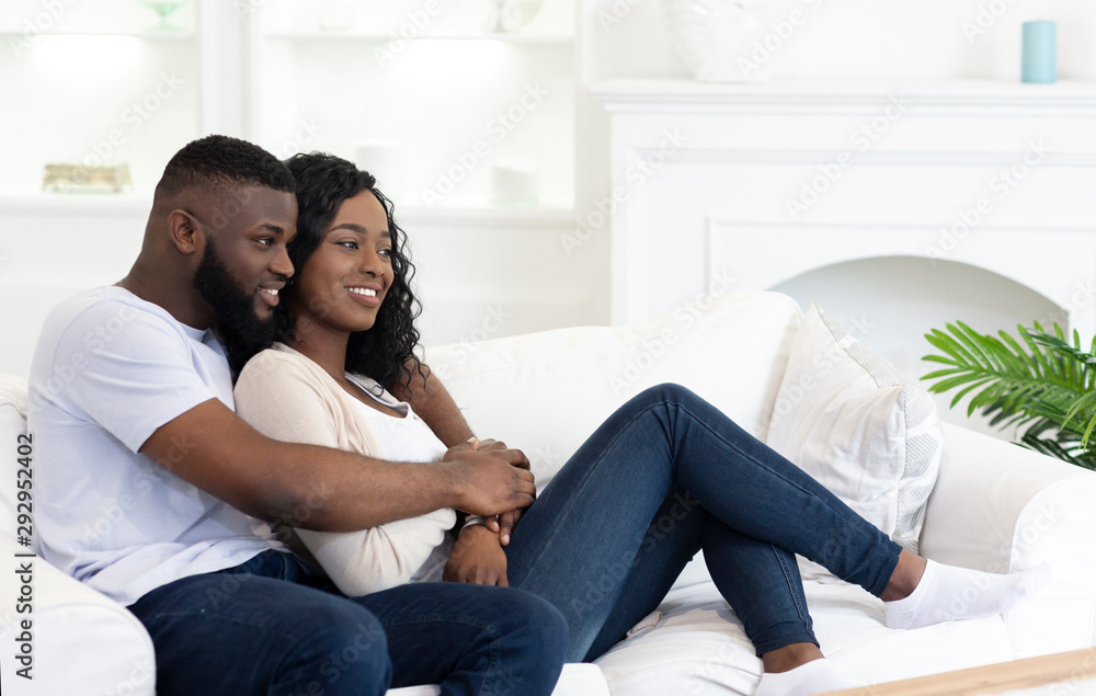 Happy black couple hugging while sitting on couch at home Stock Photo |  Adobe Stock