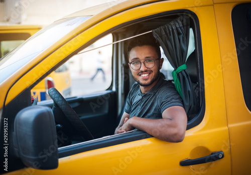 The taxi driver smiles happily, sitting in the cab of a yellow car