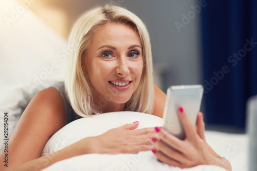 Adult beautiful woman waking up fully rested and using smartphone
