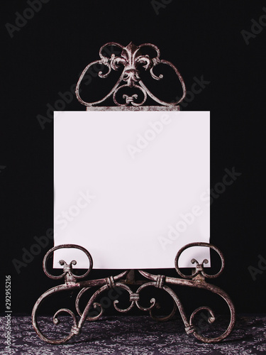 Decorative metal holder with blank paper for advertising, black background, vintage style.