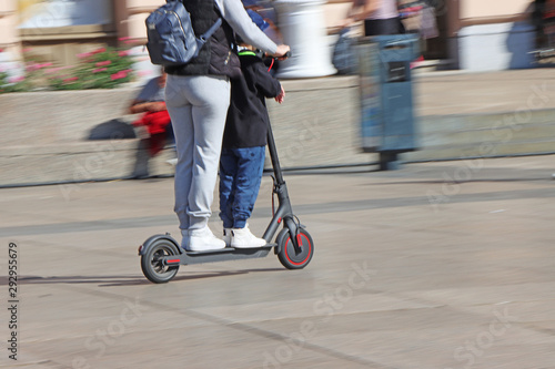 Mother and son riding electric kick scooter at the city square