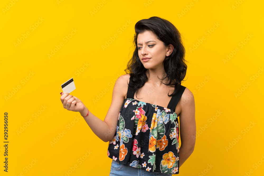 Young woman over isolated yellow background holding a credit card Young woman over isolated yellow background holding a credit card