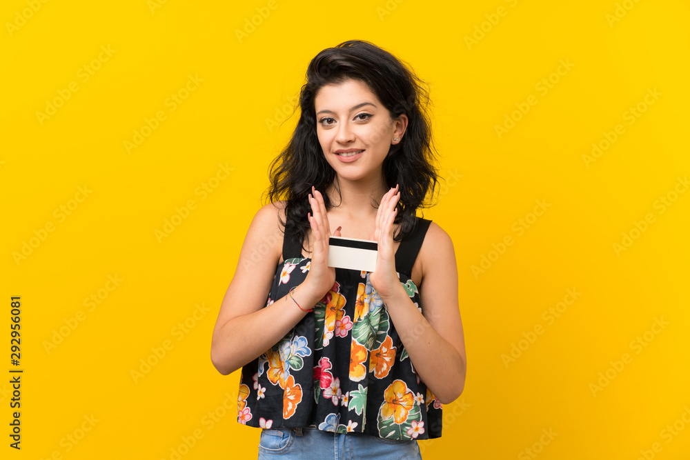 Young woman over isolated yellow background holding a credit card Young woman over isolated yellow background holding a credit card