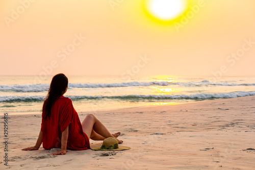 Woman sitting on sand with swimwear admiring sunset on the beach. © Julio Ricco