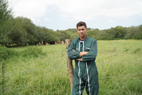 Tela Breeder standing by fence, cattle in background