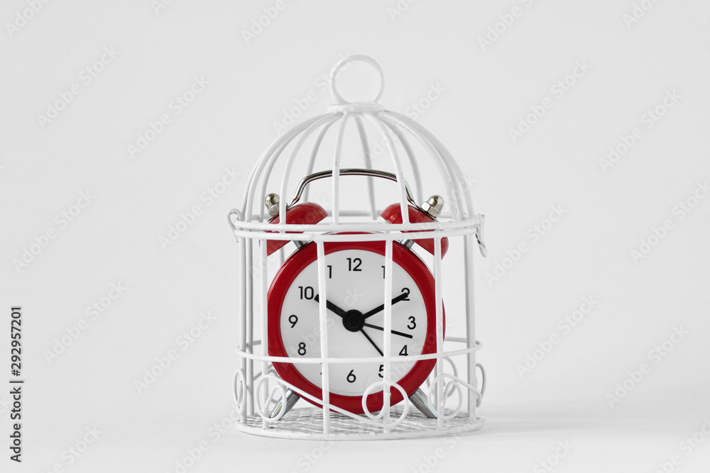 Red alarm clock in a cage on white background - Concept of time limit - obrazy, fototapety, plakaty 