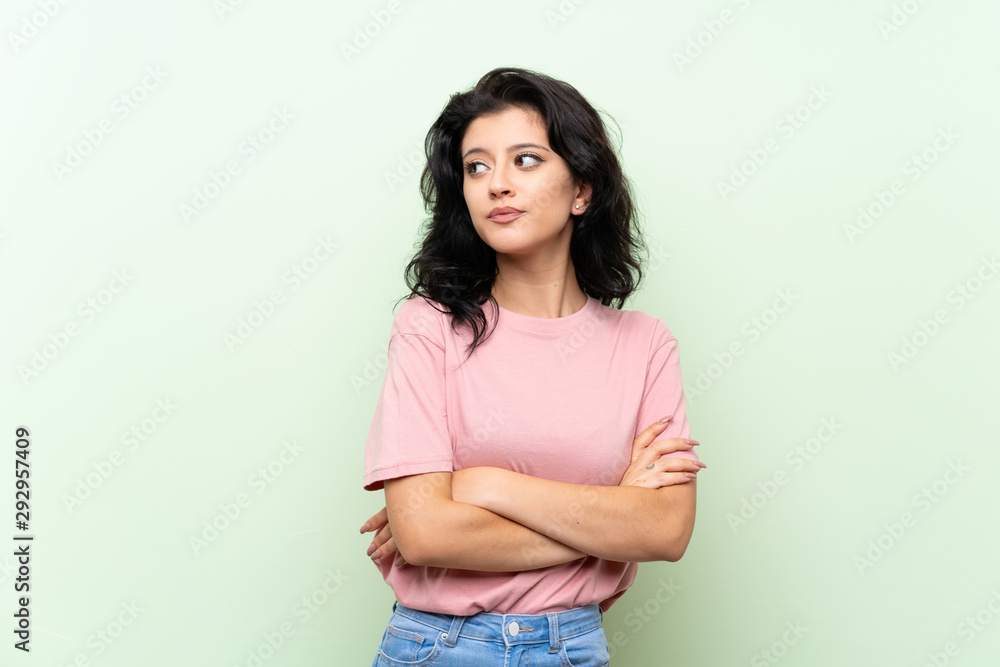 Young woman over isolated green background with confuse face expression Young woman over isolated green background with confuse face expression