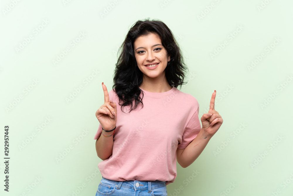 Young woman over isolated green background pointing up a great idea Young woman over isolated green background pointing up a great idea