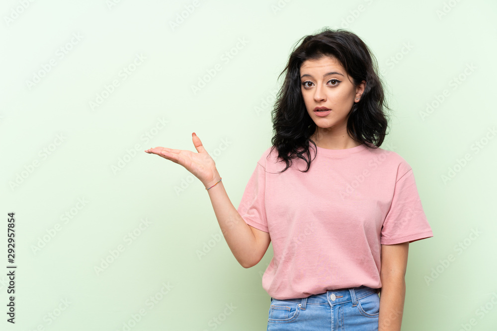 Young woman over isolated green background making doubts gesture Young woman over isolated green background making doubts gesture