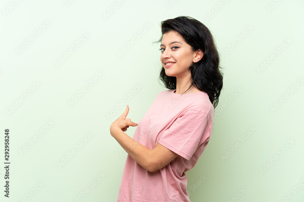 Young woman over isolated green background pointing back Young woman over isolated green background pointing back