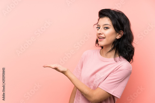 Young woman over isolated pink background extending hands to the side for inviting to come © luismolinero