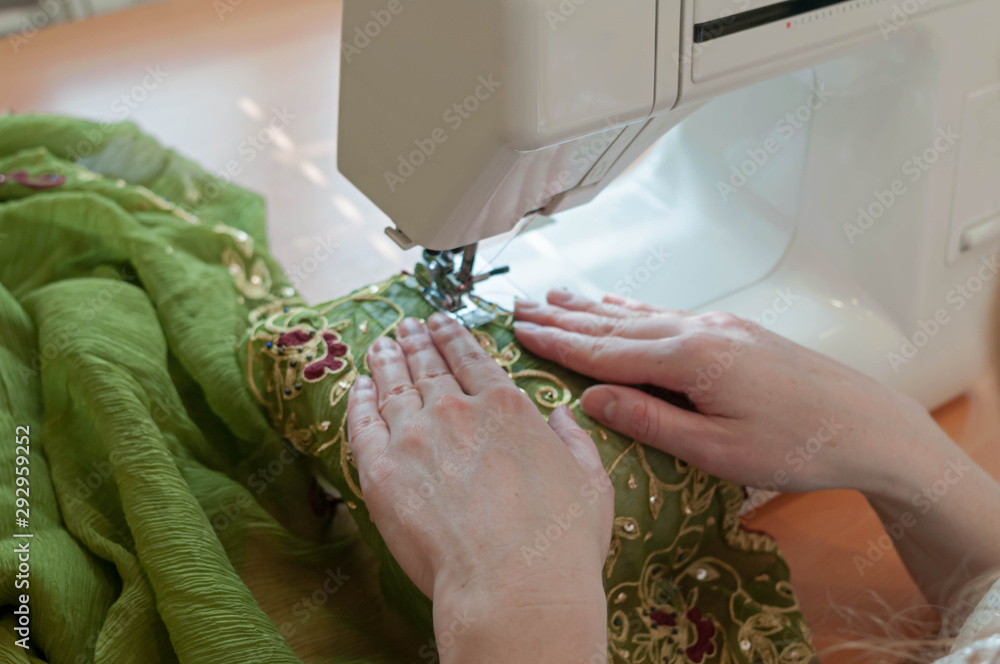 cropped view of seamstress tailoring green cloth with sawing machine at table in studio