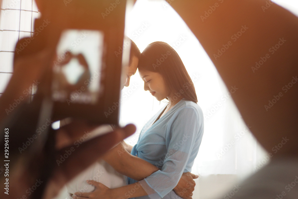 Behind the scene of photographer shooting photo of couple standing and cuddling each other with white curtains background for love and wedding shot. Lifestyle and happiness of husband and wife concept