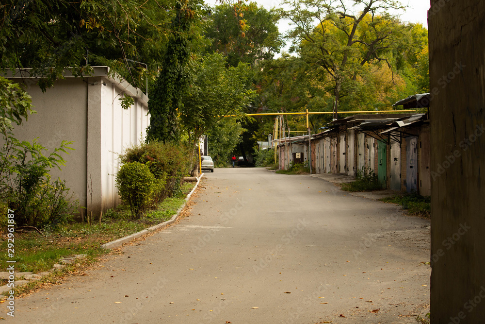 Cozy street with alley of garages and green trees, autumn weather