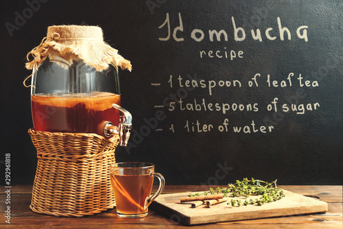 Fresh homemade kombucha fermented tea drink in a jar with faucet and in a cup and recipe on a dark wall photo