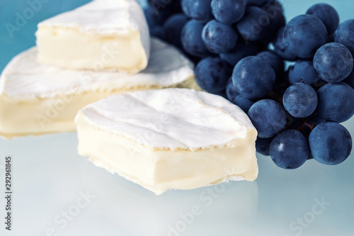 White Camembert cheese, melted cheese with mold, cheese and grapes on a light blue background