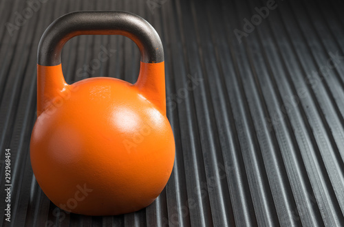 Orange 28kg weight lifting kettlebell inside a gym. Copy space to the right of kettlebell.