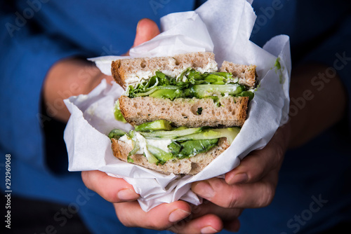 Woman's hand holding a sandwich filled with fresh salad, cucumber and avocado. Gourmet conception.