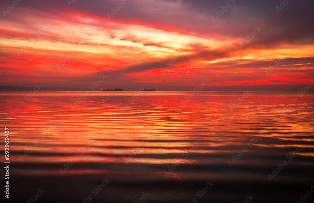 Fiery dramatic landscape with the sea, beautiful sky and ships. Dawn. small waves, almost calm.