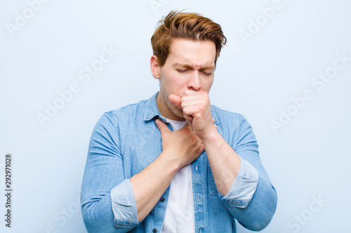 Fototapeta young red head man feeling ill with a sore throat and flu symptoms, coughing wit