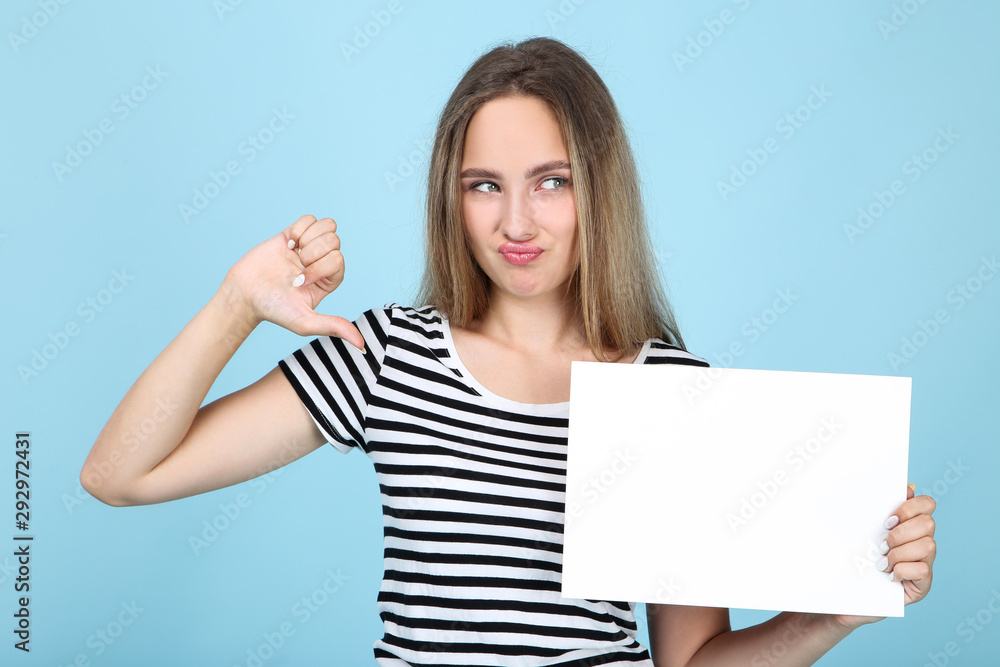 Beautiful young woman holding white blank board and showing thumb down on blue background Beautiful young woman holding white blank board and showing thumb down on blue background