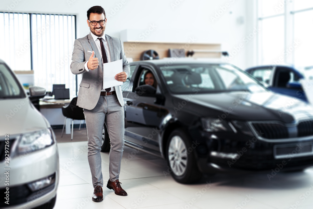 Professional car dealer posing proudly at auto showroom.