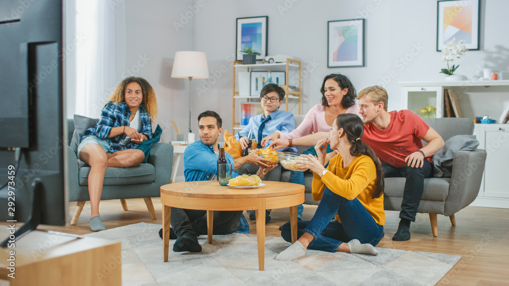At Home Diverse Group Friends Watching TV Together, Eating Snacks and Drinking Beverage. They Probably Watching Sports Game or a Movies. At Home Diverse Group Friends Watching TV Together, Eating Snacks and Drinking Beverage. They Probably Watching Sports Game or a Movies.
