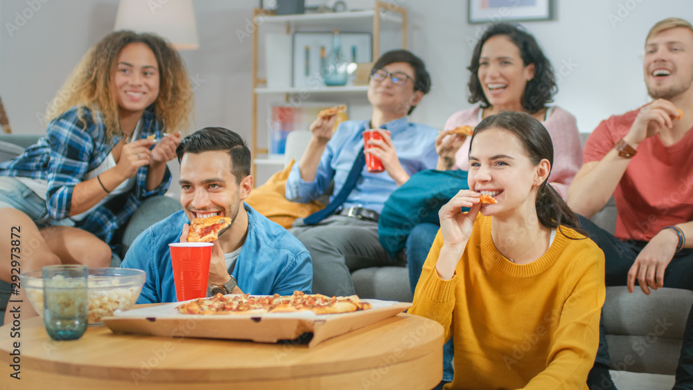 Fototapeta premium At Home Diverse Group Friends Watching TV Together, They Share Gigantic Pizza, Eating Tasty Pie Pieces. Guys and Girls Watching Comedy Sitcom or a Movie, Laughing and Having Fun Together.