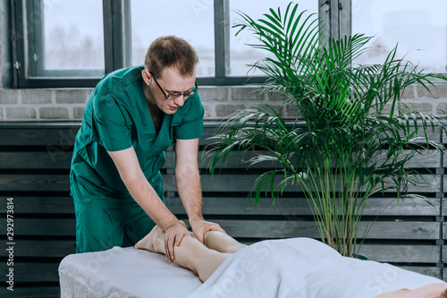 A male massage therapist massages the feet and legs of female legs. Lymphatic drainage massage