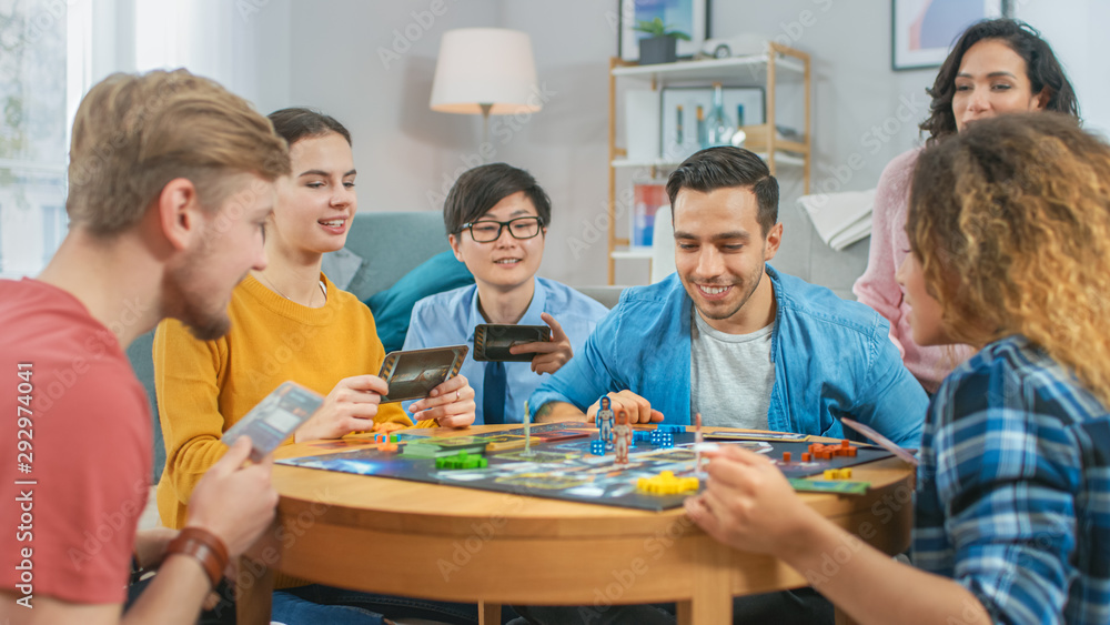 Diverse Group of Guys and Girls Playing in a Strategic Board Game with Cards and Dice. Cozy Living Room in a Daytime - obrazy, fototapety, plakaty 