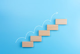 Wooden block stacking as step stair with white arrow up on blue background, Ladder of success in business growth concept, copy space