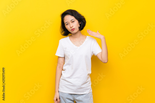 Asian young woman over isolated yellow wall with tired and sick expression © luismolinero
