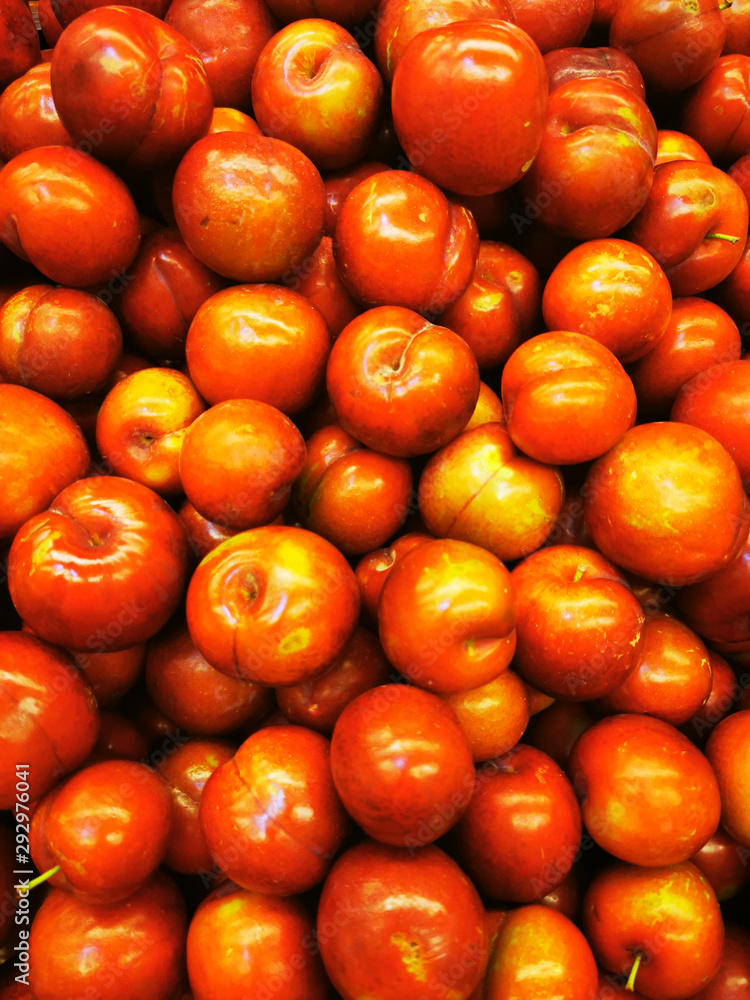 Ripe red greengages in a pile on a market.