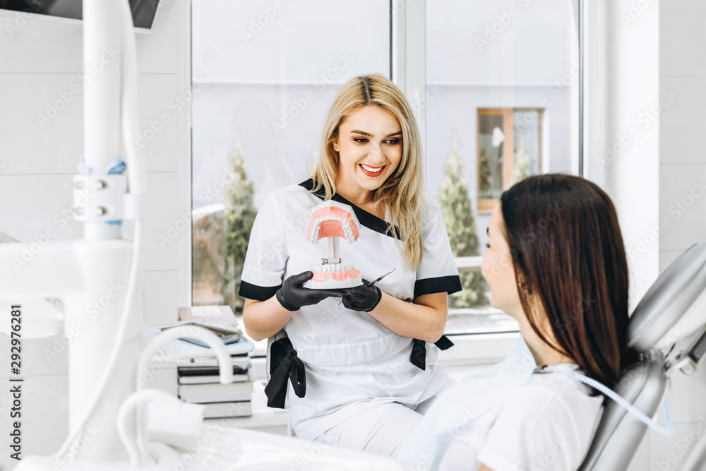 Pretty female dentist explaining way of treatment on the denture for the patient in the clinic. Pretty female dentist explaining way of treatment on the denture for the patient in the clinic.